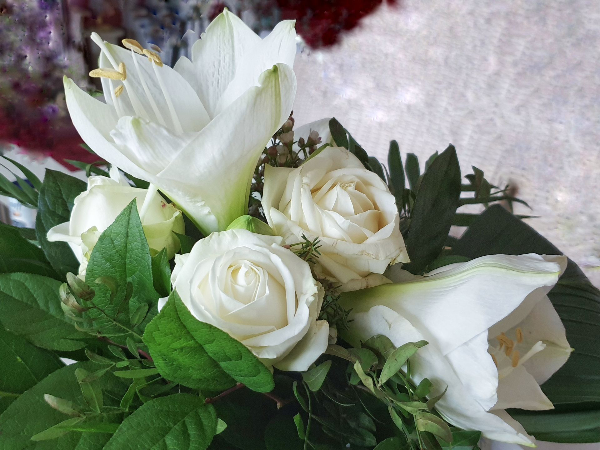 White roses and lilies in a floral arrangement with green foliage.