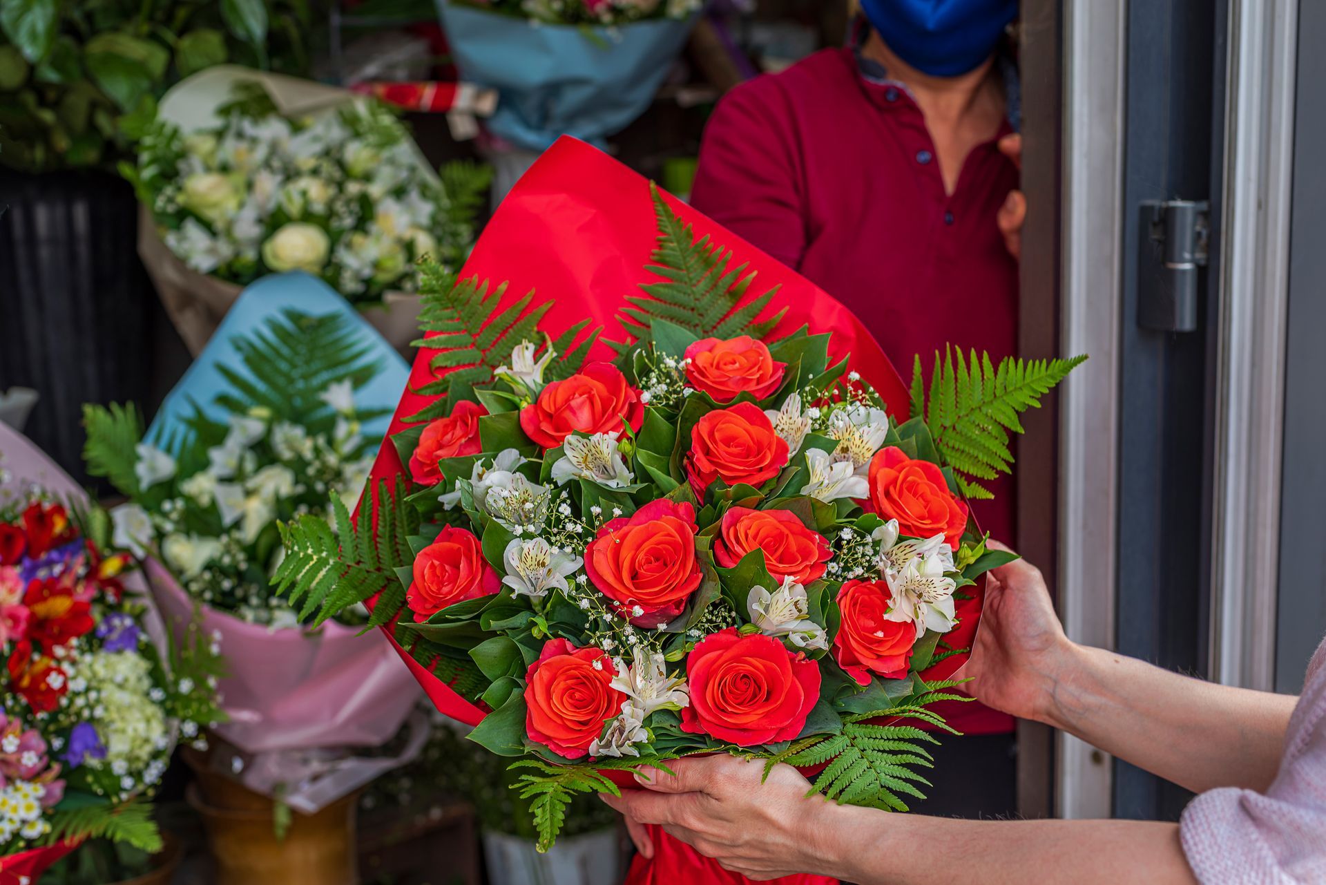 Person holding a bouquet of red roses and white flowers in a flower shop.
