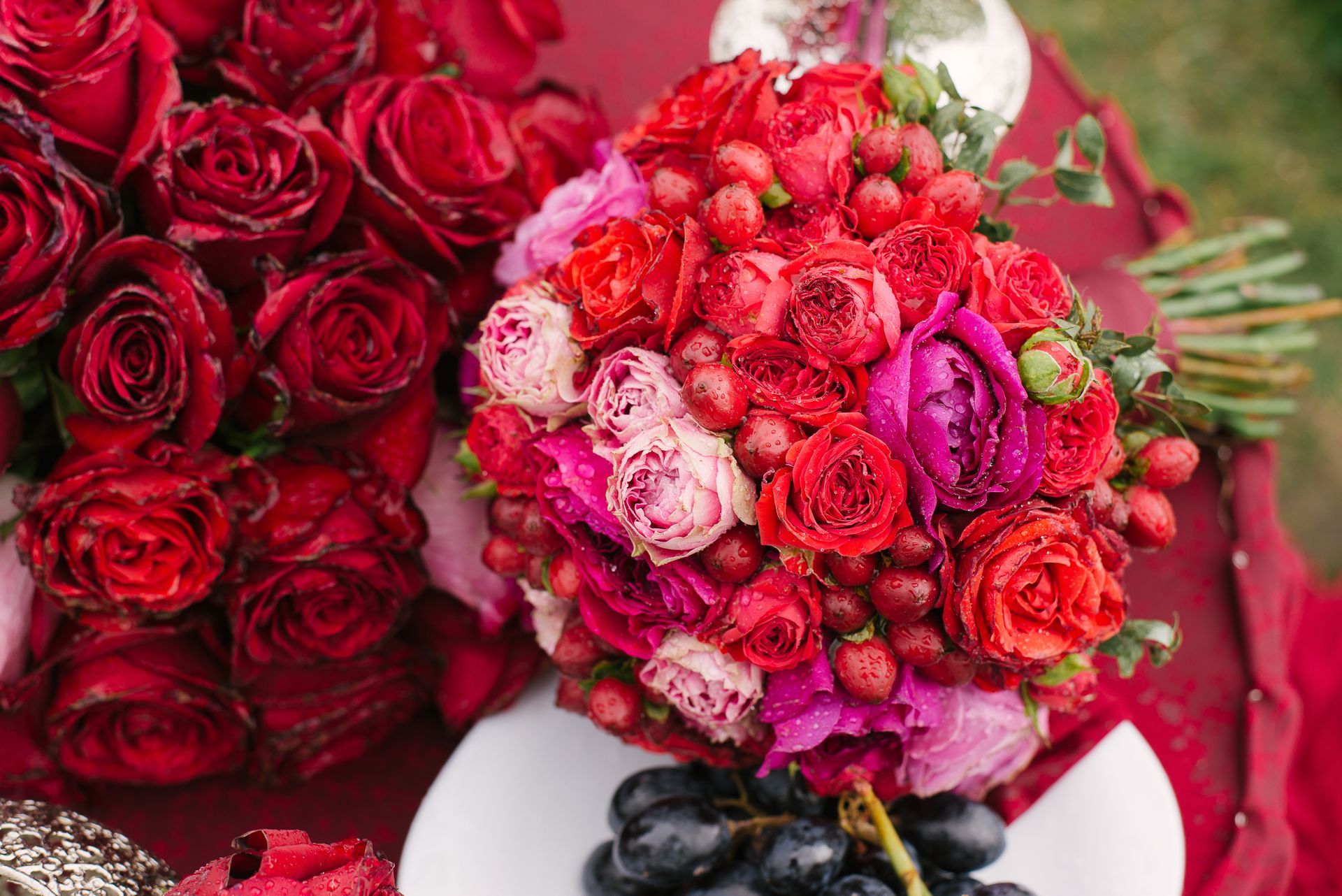 Bouquet of red and pink roses with grapes on a white plate.
