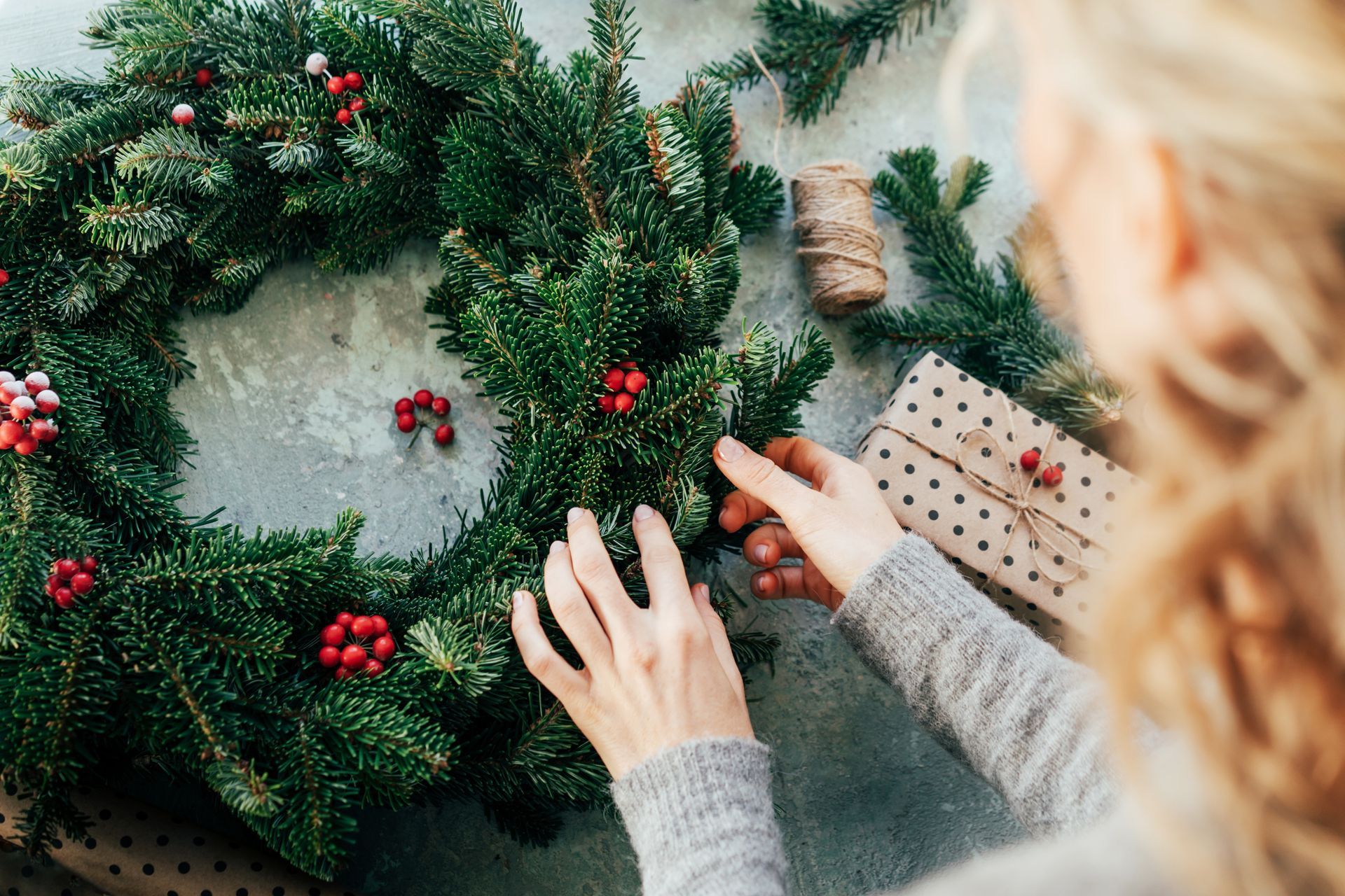 A woman is making a christmas wreath on a table.