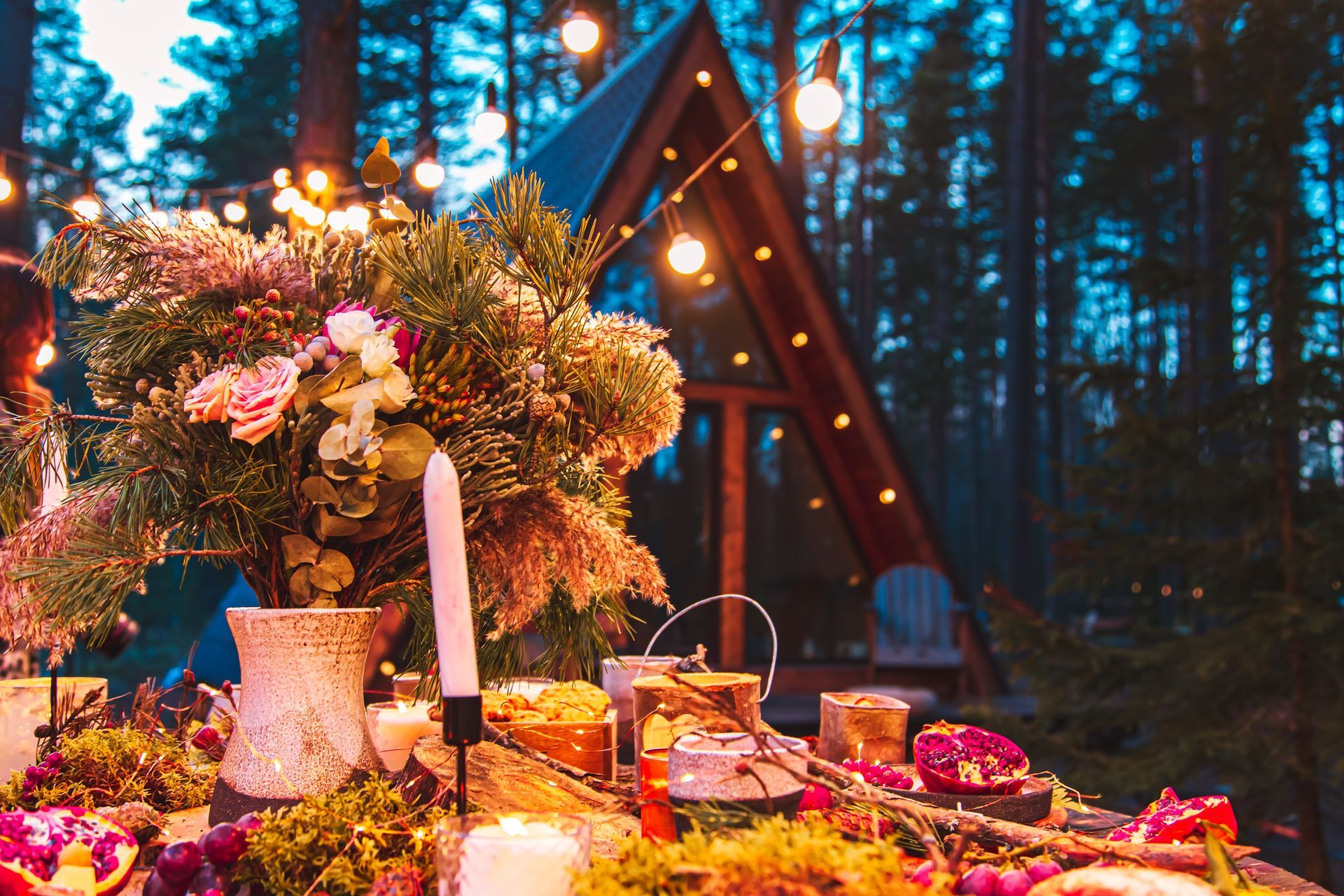 A table with flowers and candles in front of a tent in the woods.