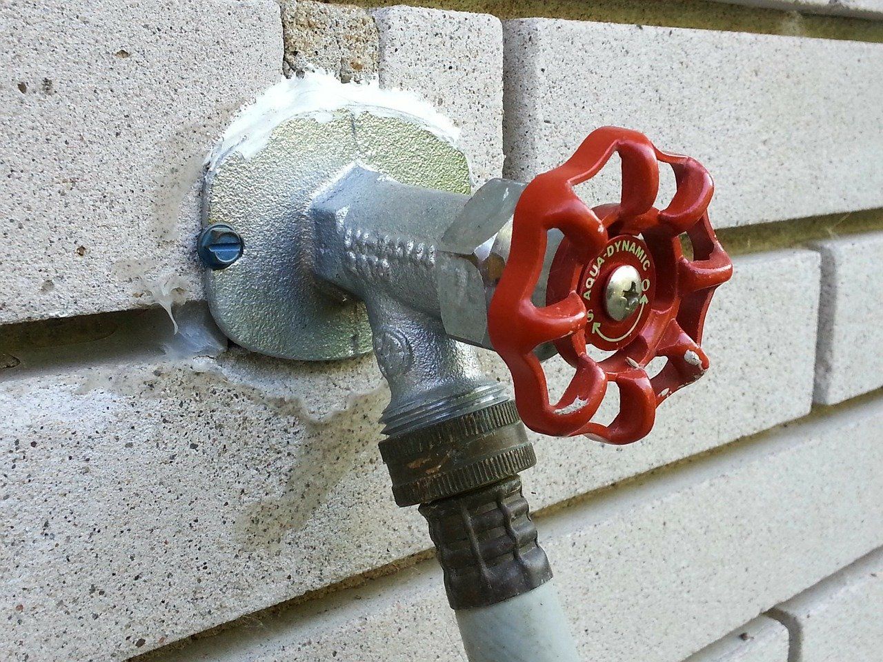 Water pipe on the outside of a brick building with red handle