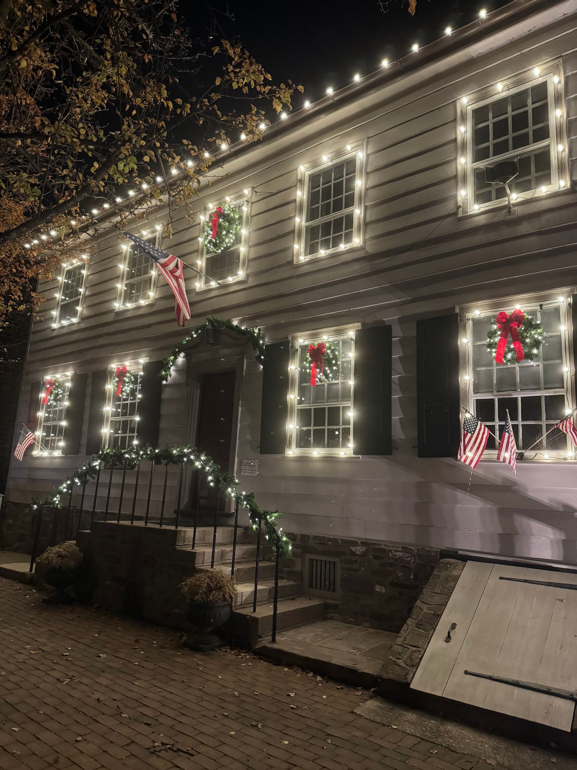 A two-story white building with Christmas lights, wreaths, and an American flag at night.