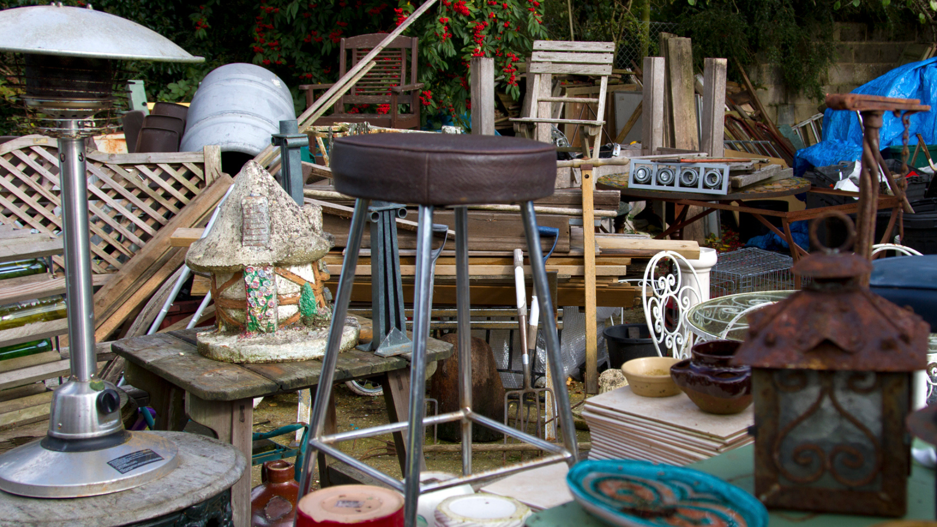 Yard sale with various items: bar stool, heater, lamps, furniture, and other objects.