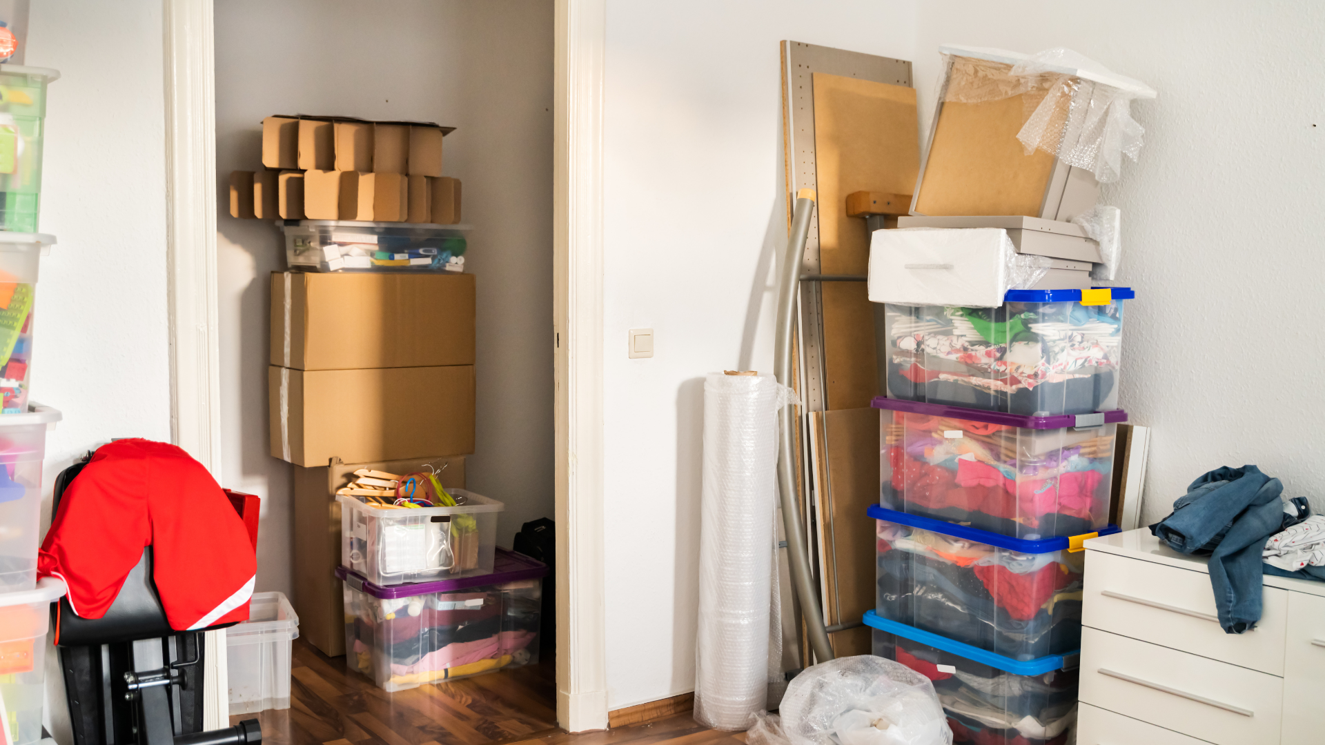 Room overflowing with stacked cardboard boxes and plastic bins, items piled in a doorway.