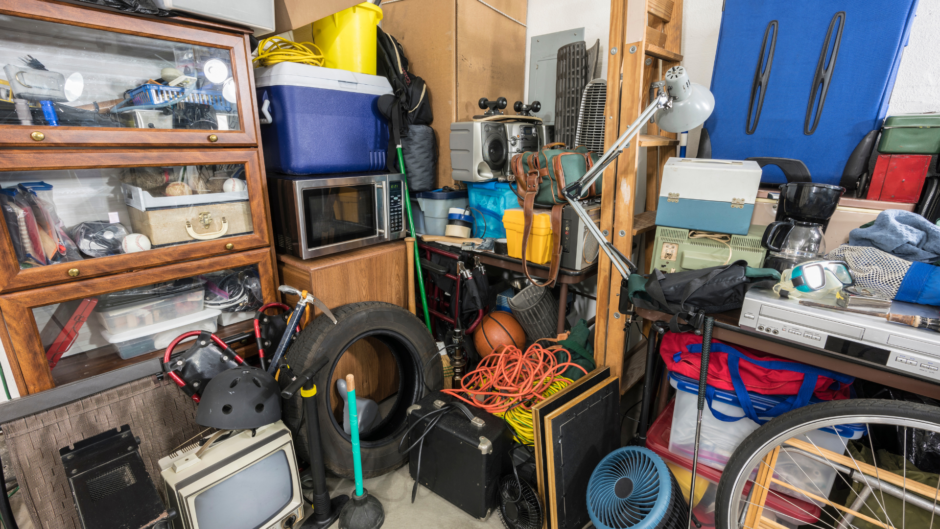 Cluttered garage; various items include a microwave, tires, a cabinet, and boxes stacked together.