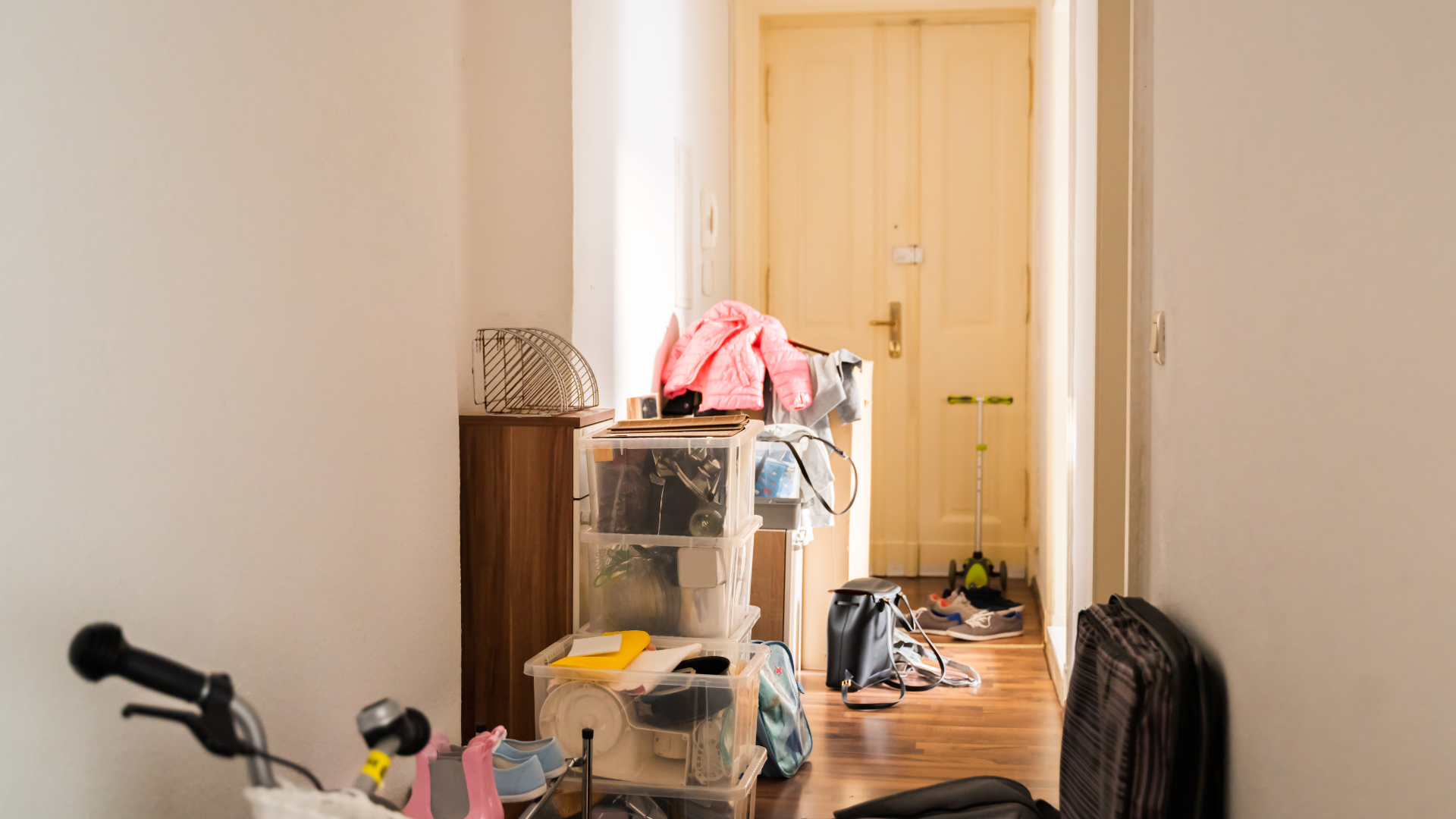 Cluttered hallway with a plastic storage unit, clothes, and a bicycle. Door at the end.