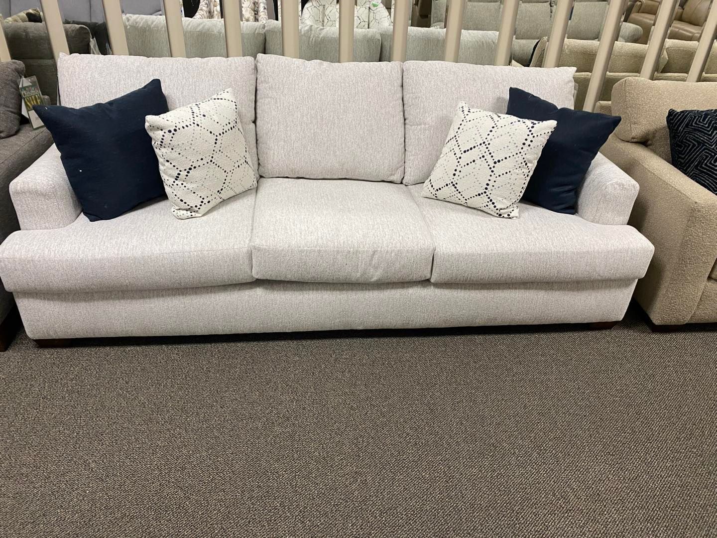 A white couch with blue pillows on it is sitting on a carpet in a living room.