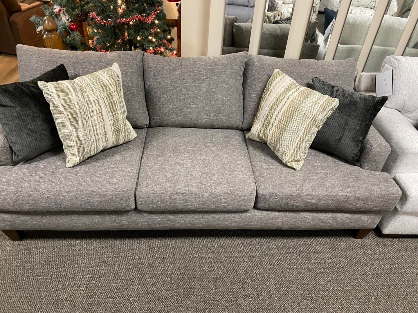 A grey couch with pillows on it is sitting on a carpet in a living room.