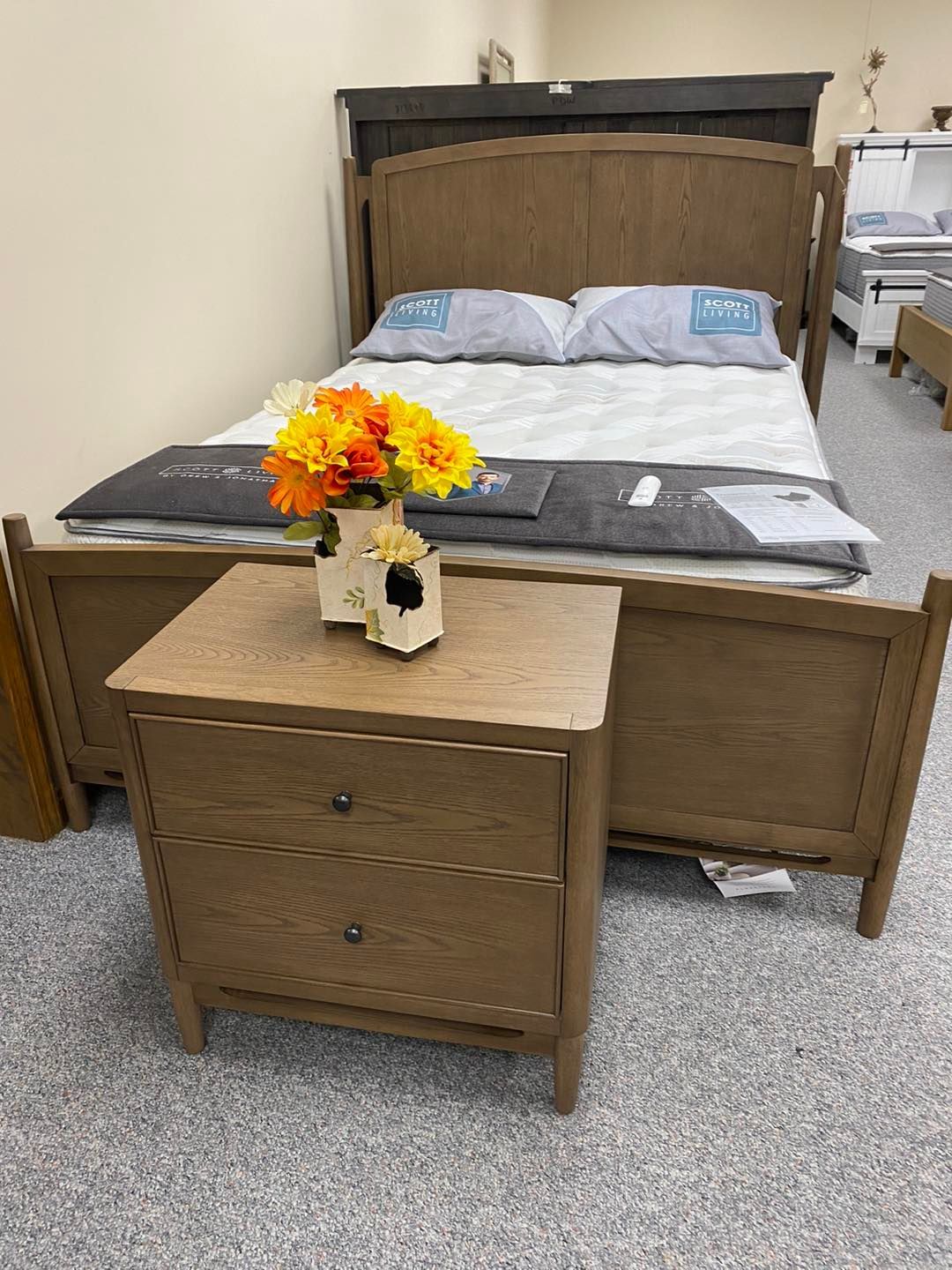 A bed with a nightstand and a vase of flowers on it.