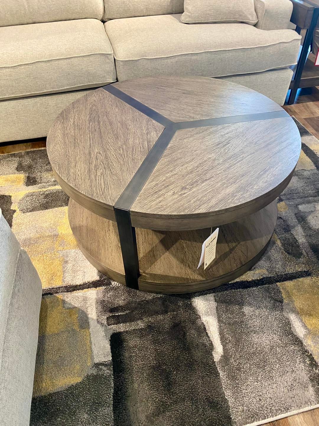 A round coffee table is sitting on top of a rug in a living room next to a couch.