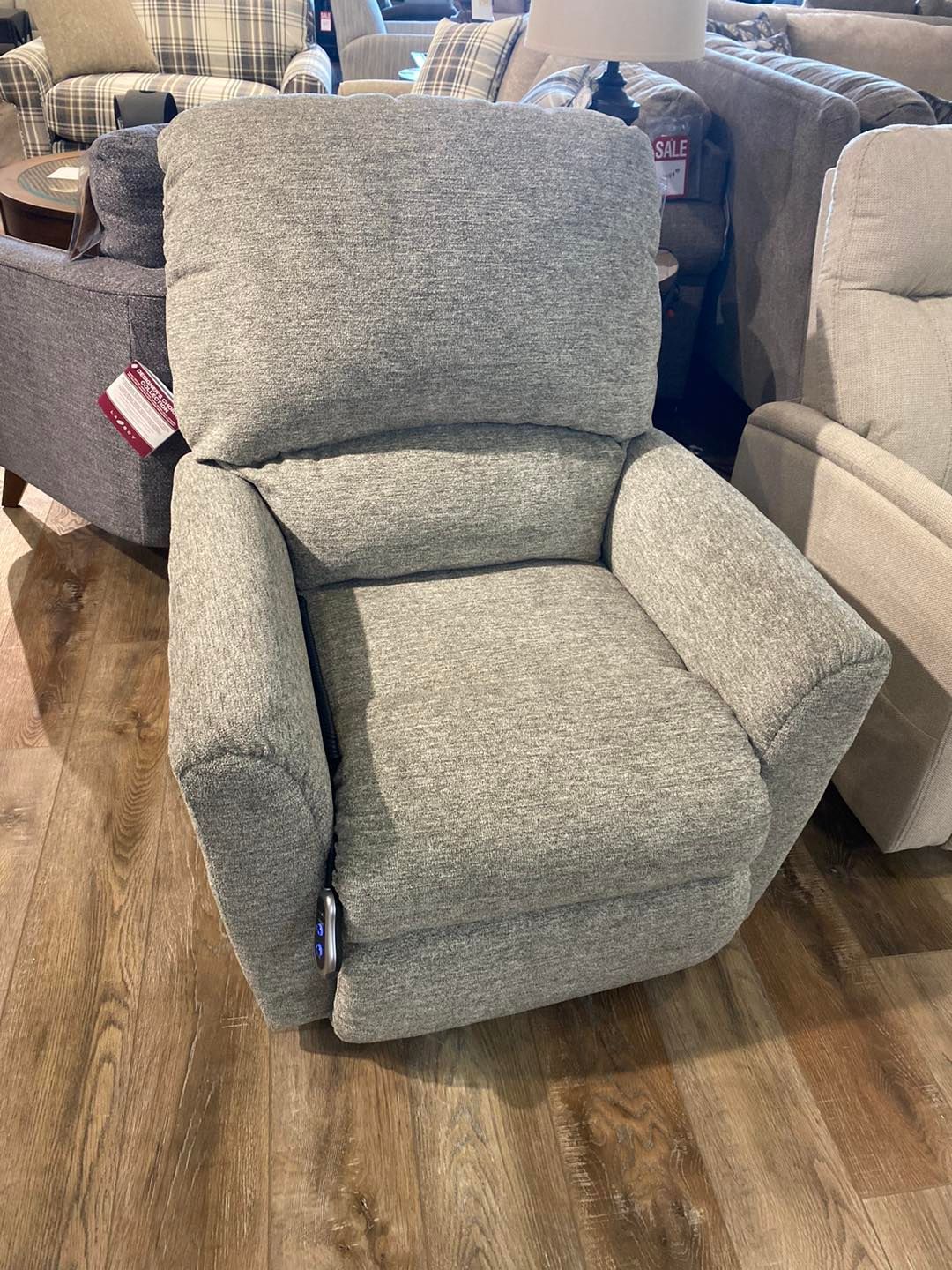 A grey recliner is sitting on a wooden floor in a living room.
