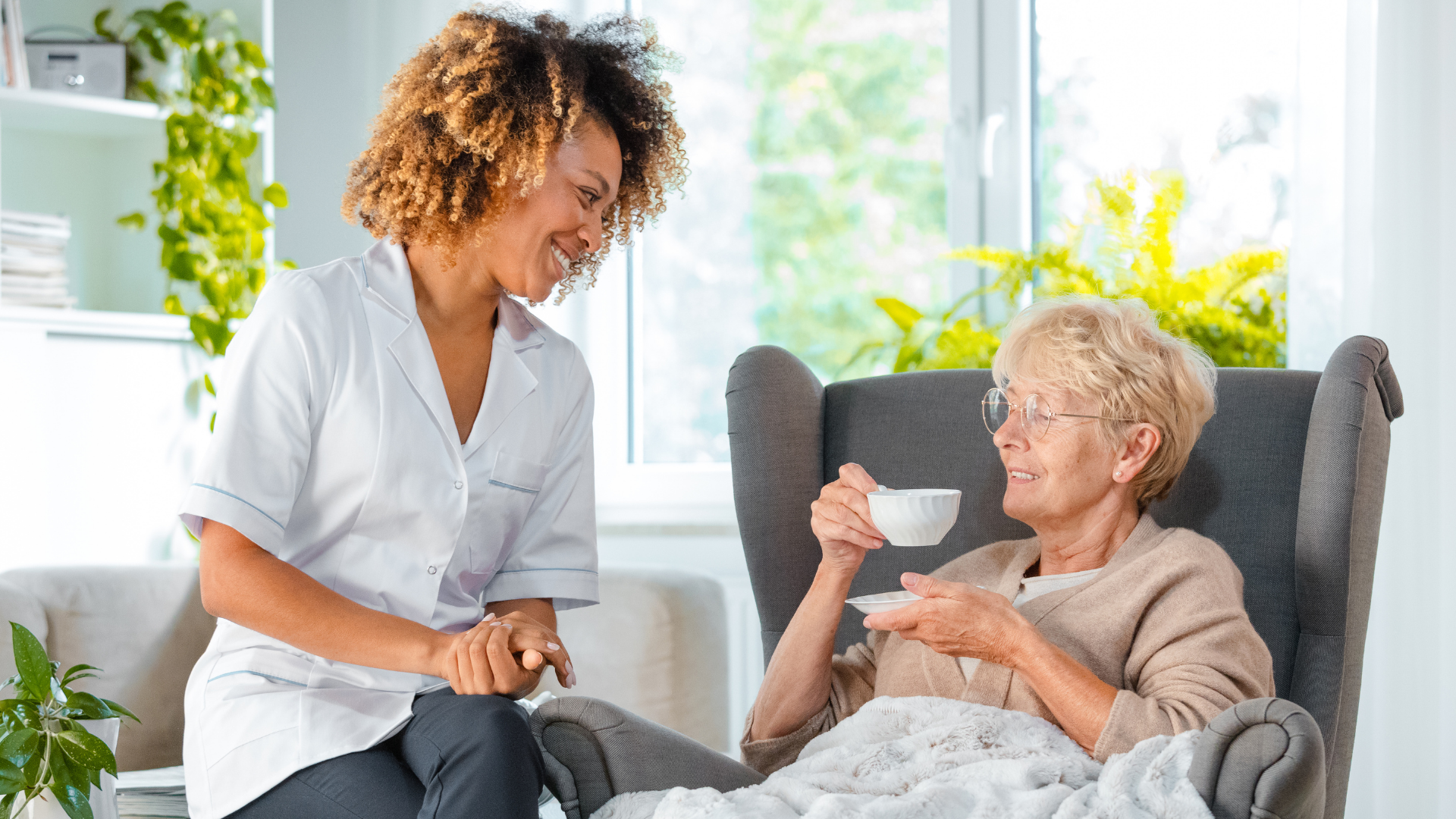 A nurse is giving an elderly woman a cup of coffee.