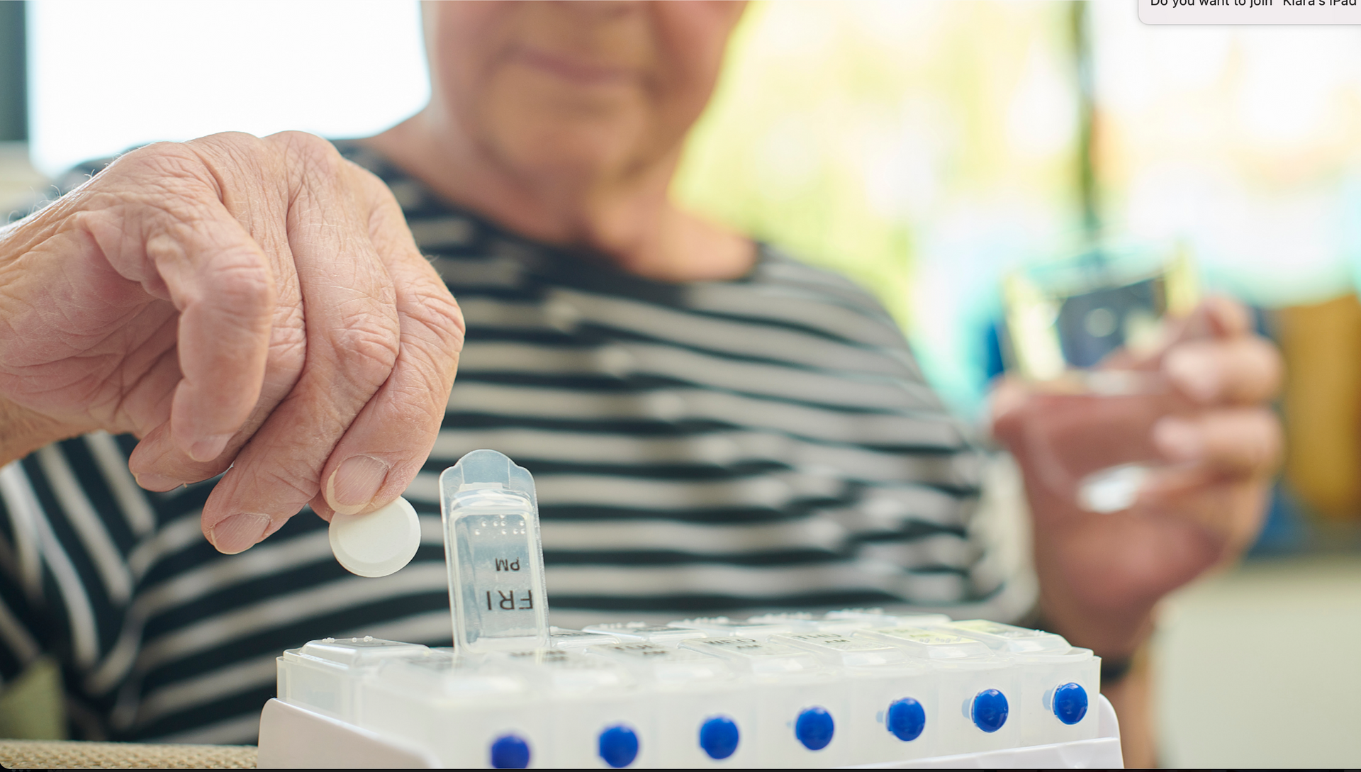 An elderly woman is taking a pill from a bottle.