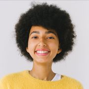 A young woman with an afro is wearing a yellow sweater and smiling.