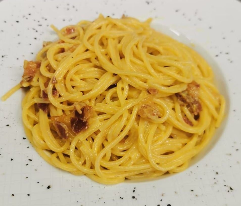 un piatto bianco condito con spaghetti e pancetta su un tavolo.