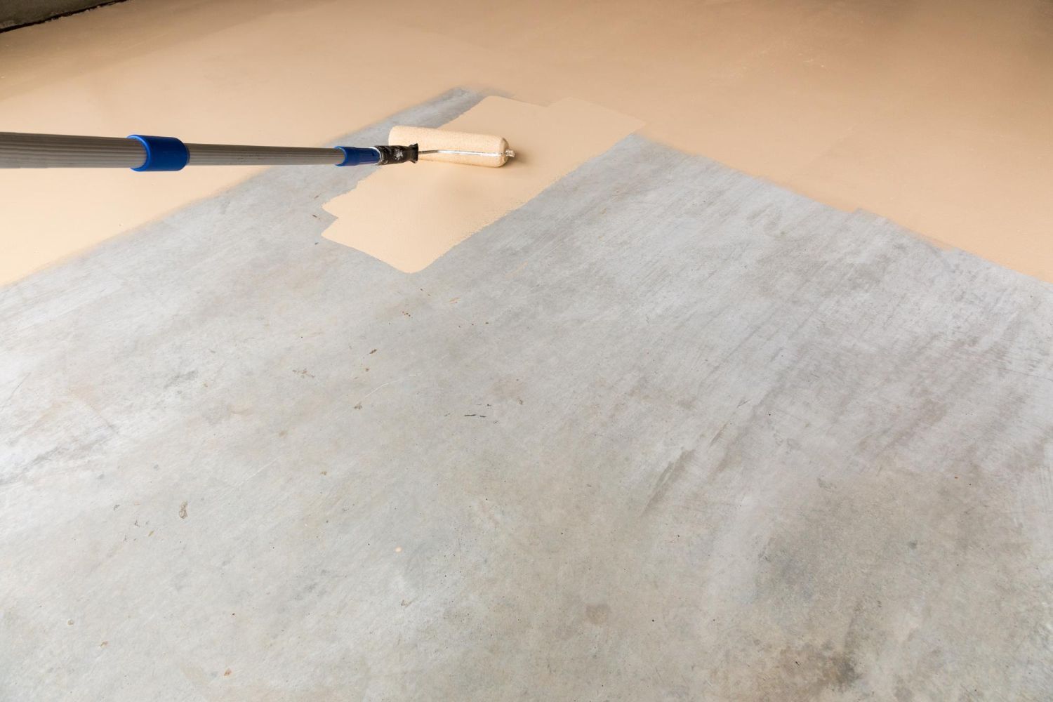 A person is painting a concrete floor with a roller.