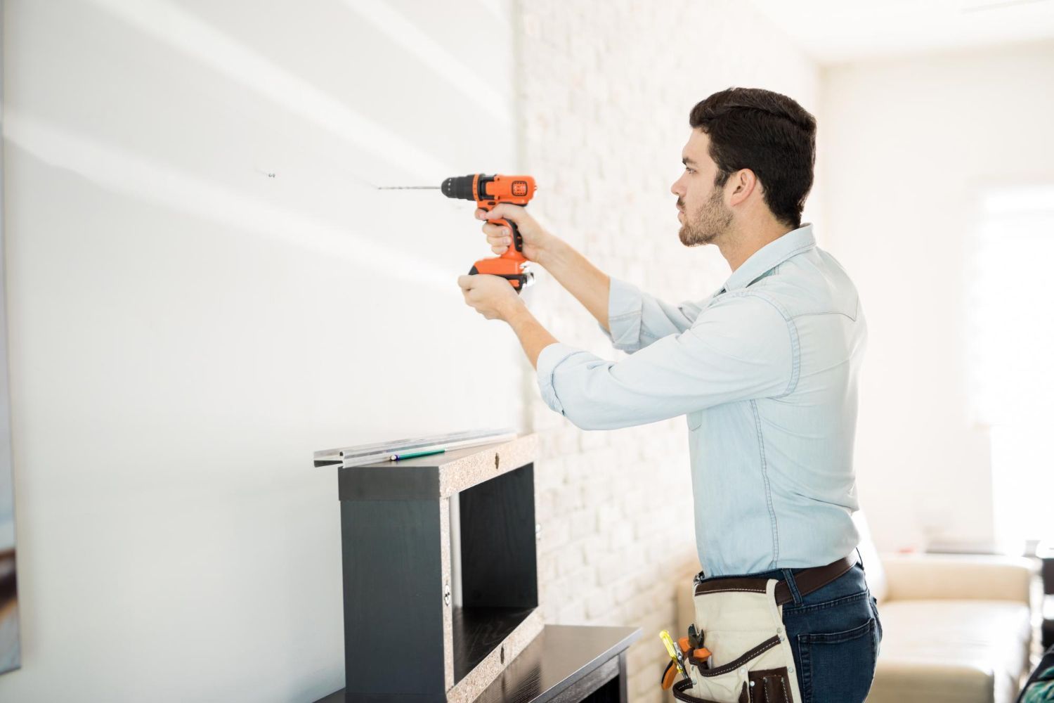 A man is using a drill to install a shelf on a wall.