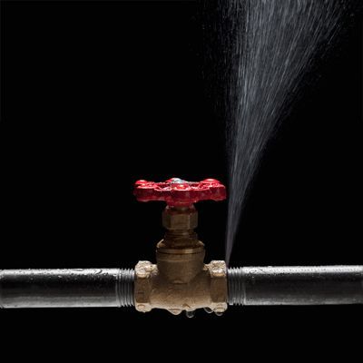 A water pipe with a red valve is leaking water.