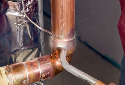 A person is welding a copper pipe with a welding iron.