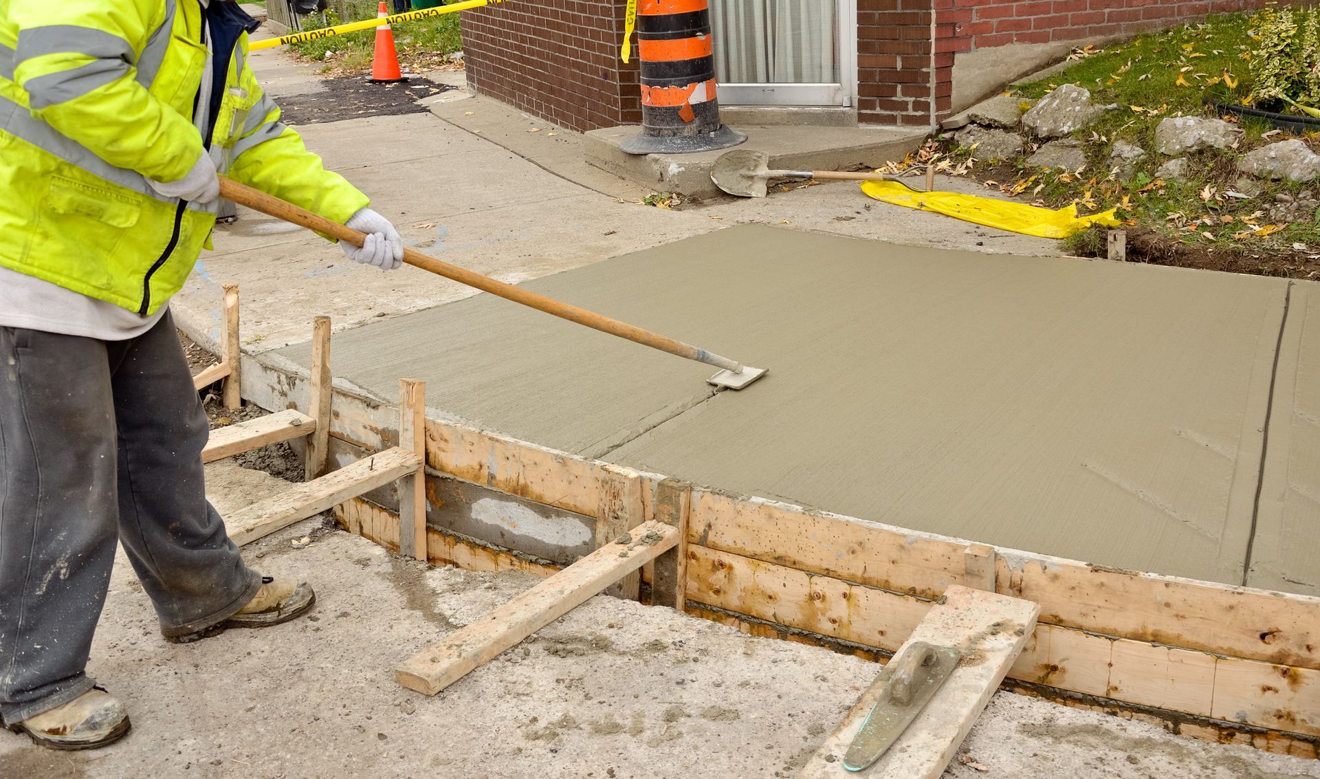Construction worker smoothing wet concrete in a sidewalk form.