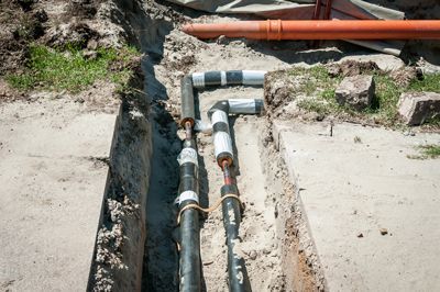 A bunch of pipes are laying in the dirt in a trench.