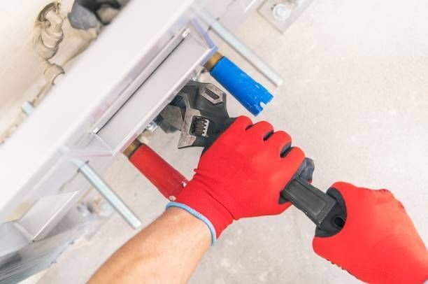 A person wearing red gloves is working on a pipe with a wrench.