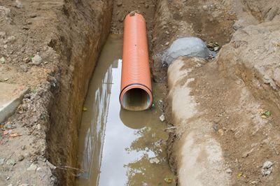 A large orange pipe is sitting in a muddy trench.