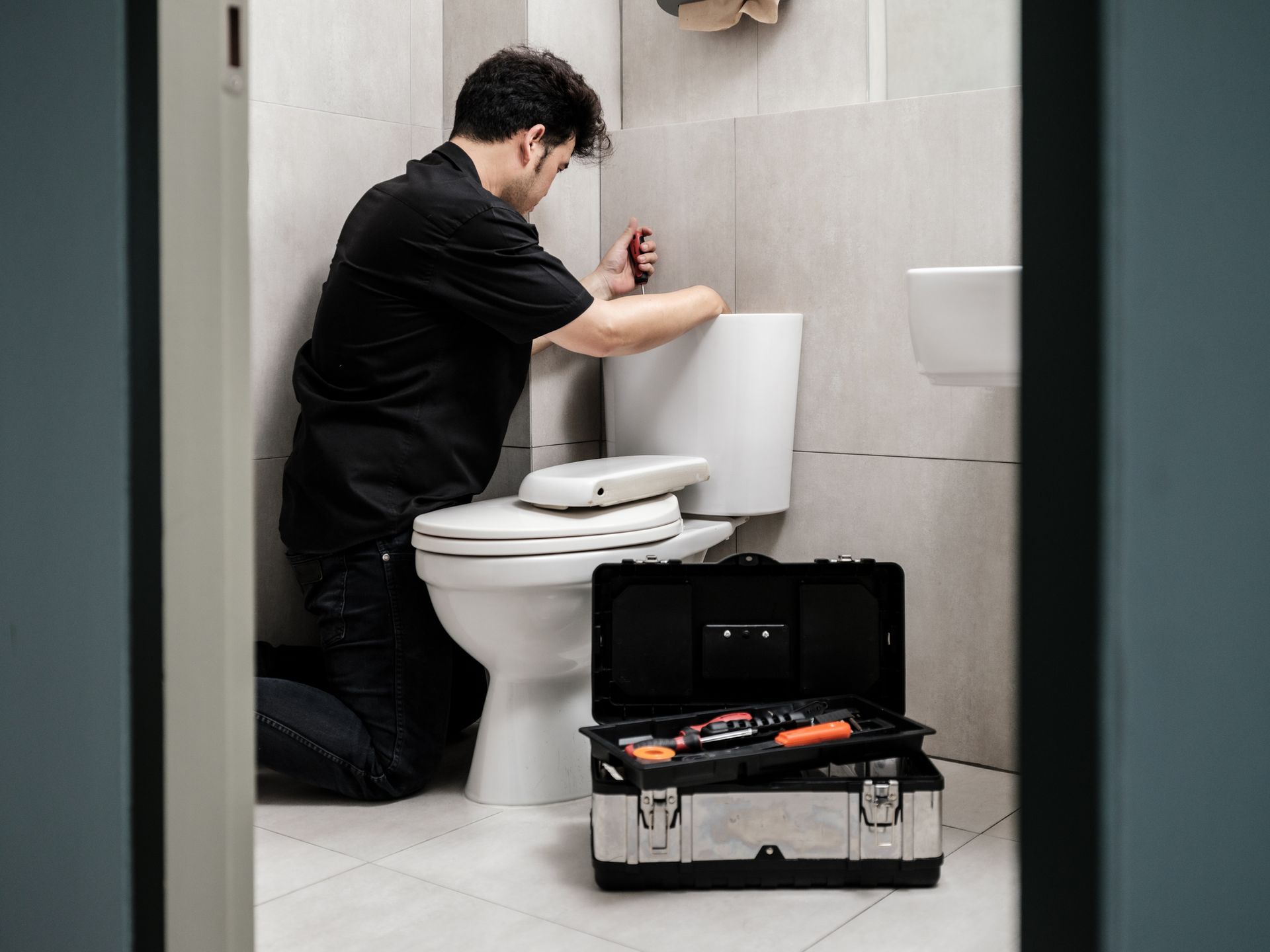 Image Tag: A man is fixing a toilet. 