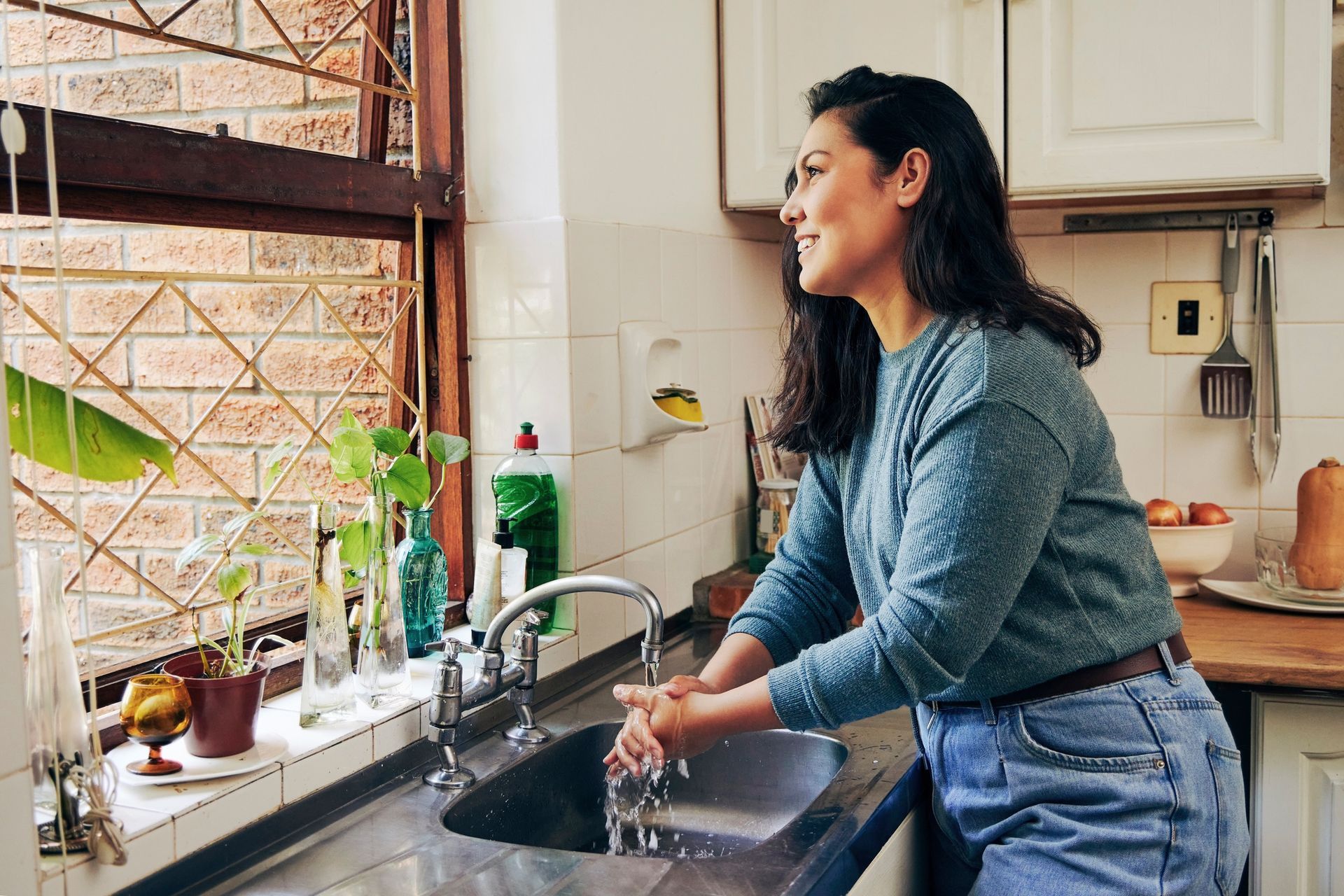 A woman is washing her hands in a kitchen sink.
