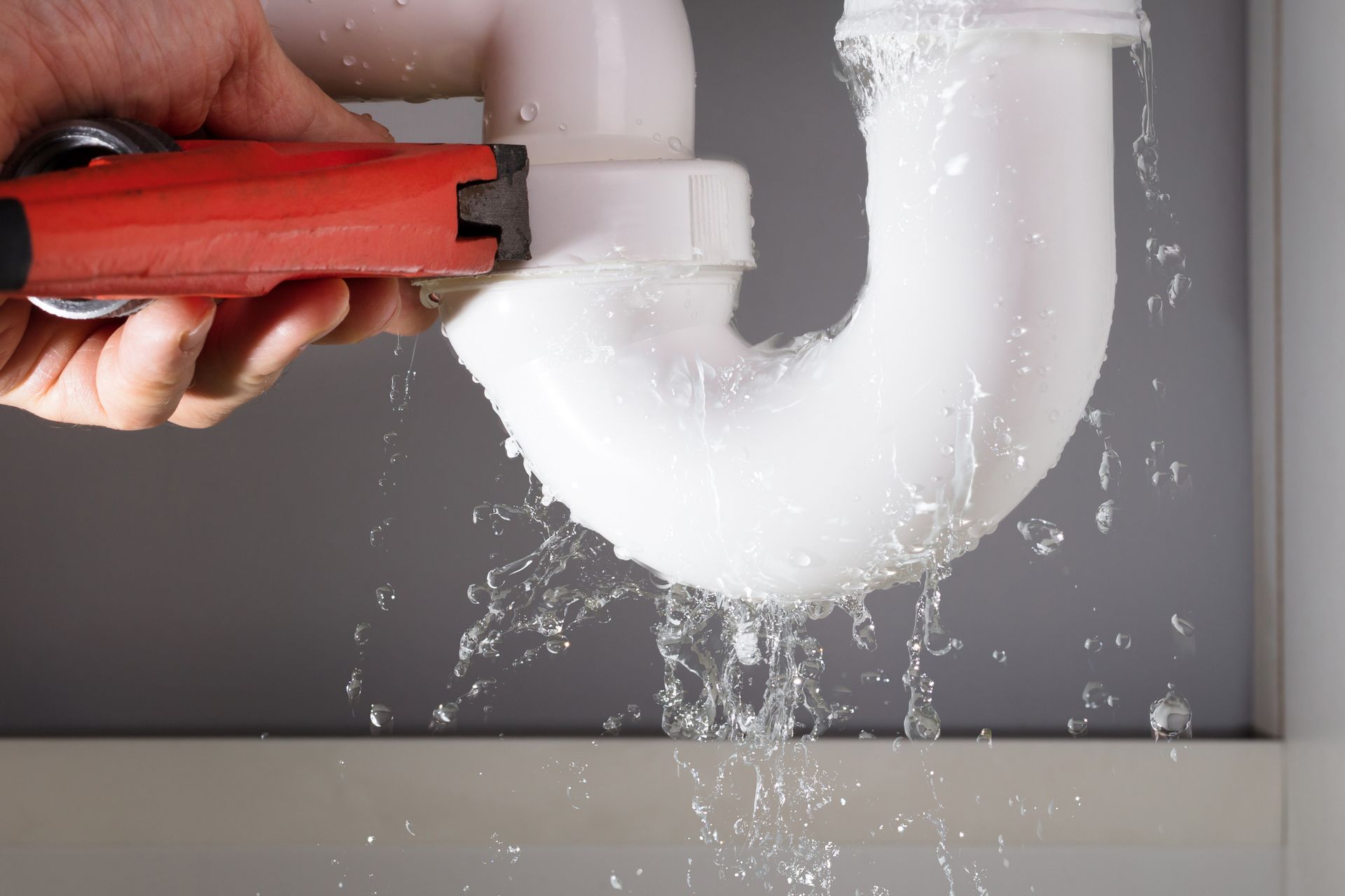 A plumber fixing a white sink pipe with a wrench, highlighting emergency plumbing services.