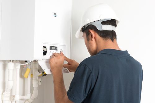 A man wearing a hard hat is working on a boiler.