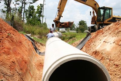A large concrete pipe is being installed in a trench