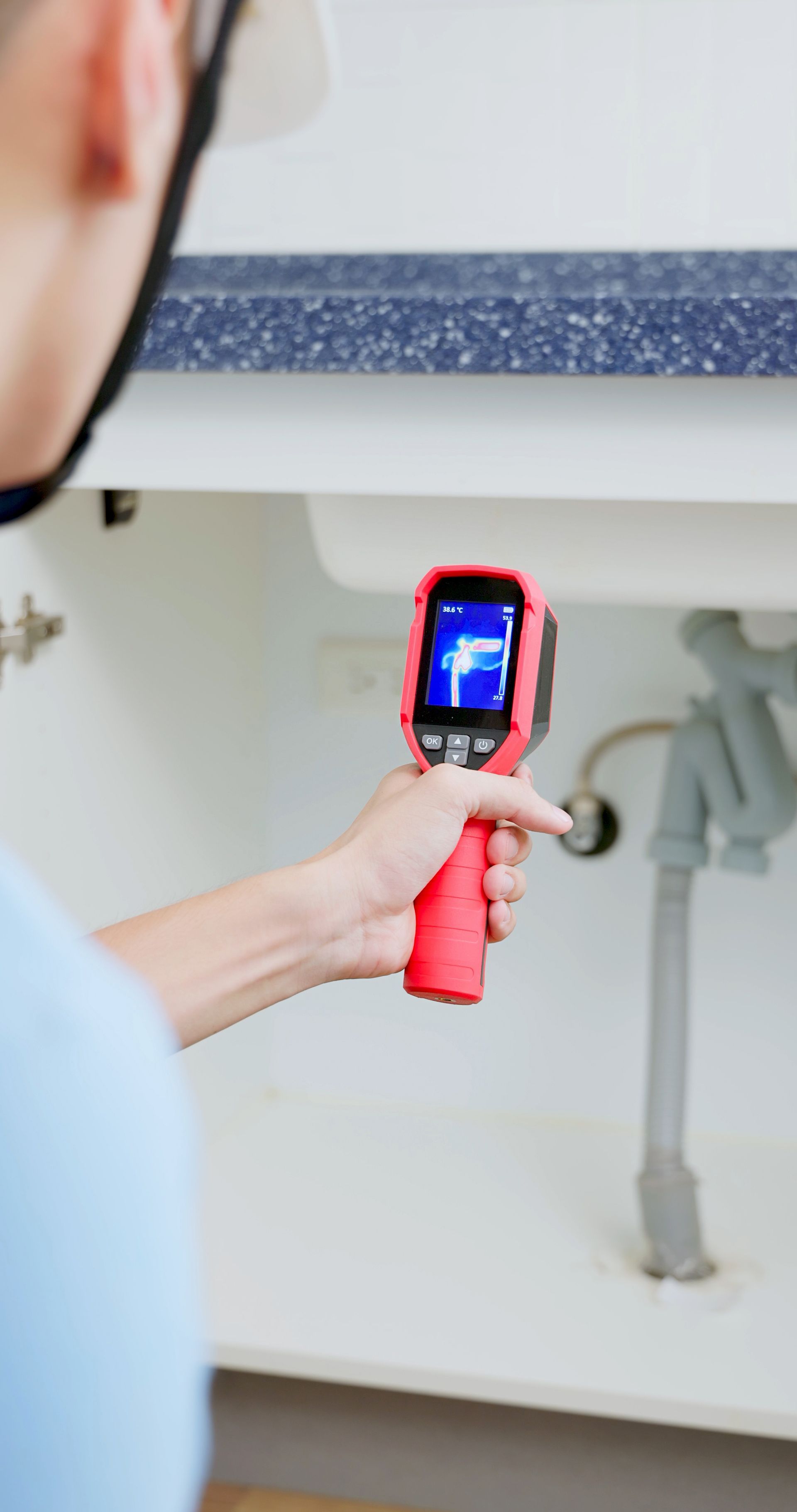 A man is using a camera to look under a sink.