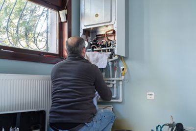 A man is kneeling down in a room fixing a boiler.