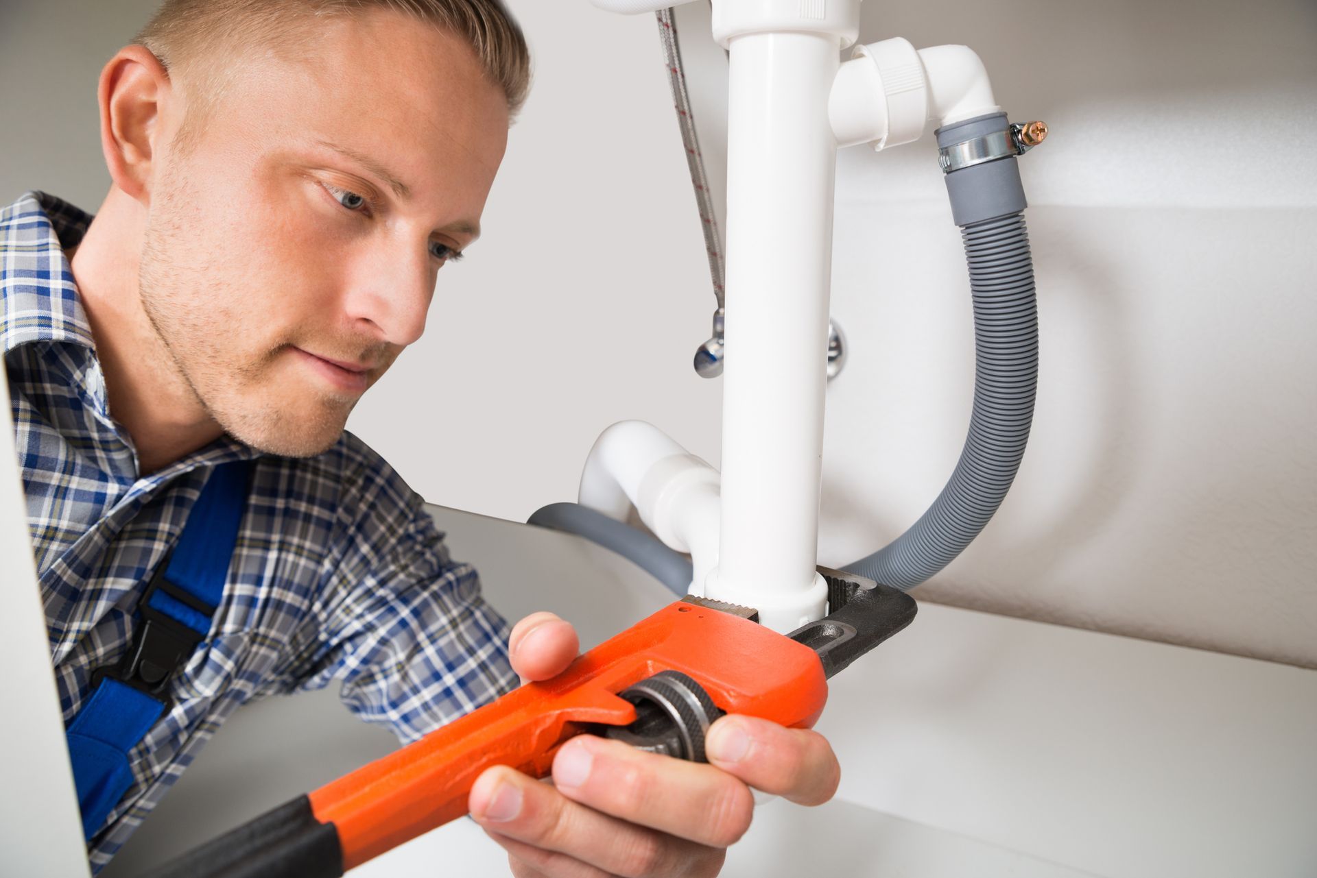 A man uses a wrench to adjust a pipe under a sink, showcasing expert emergency plumbing services.