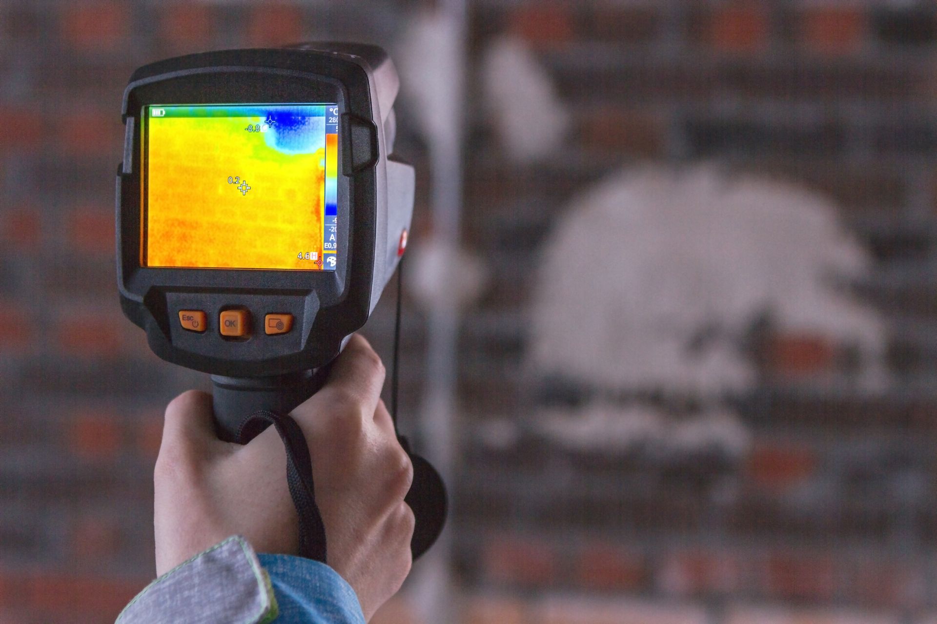 A person is holding a thermal camera in front of a brick wall.