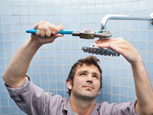A man is fixing a shower head with a wrench.