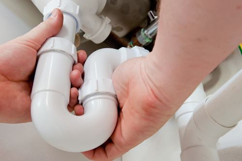 A person is fixing a sink pipe in a bathroom.