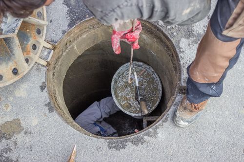 A man is standing in a manhole with a bucket in it.