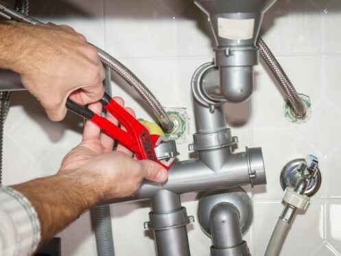 A plumber is fixing a sink pipe with a wrench.