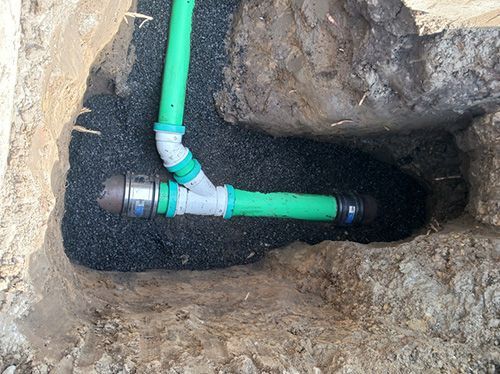 A green pipe is being installed in a hole in the ground.