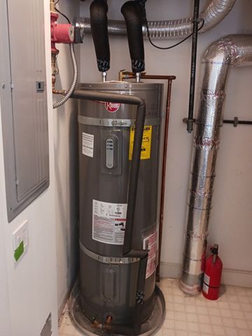 A gray water heater is sitting in a room next to a fire extinguisher.