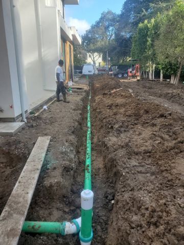 A man is standing in the dirt next to a green pipe.