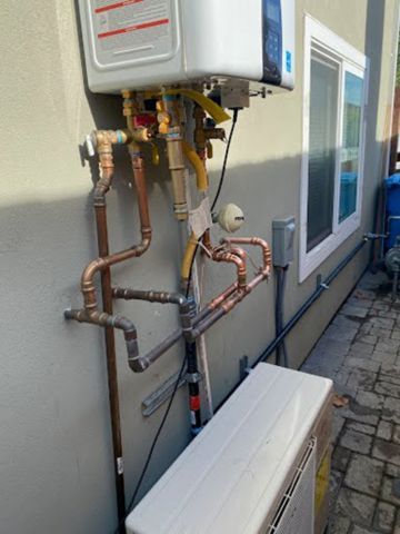 A water heater is attached to the side of a building with copper pipes.