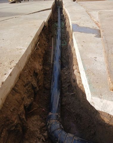 A black pipe is being installed in a trench.