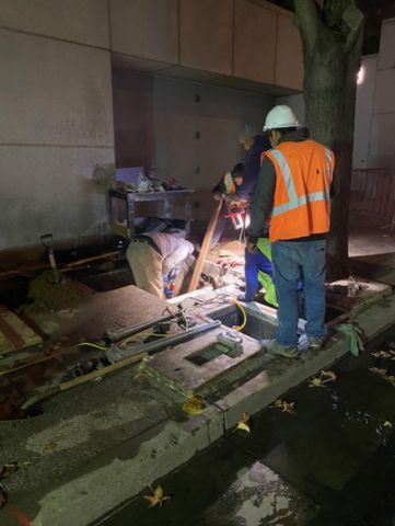 A group of construction workers are working on a sidewalk at night.