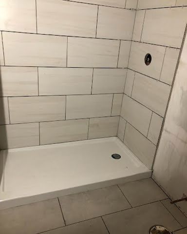 A bathroom with white tiles and a shower stall.