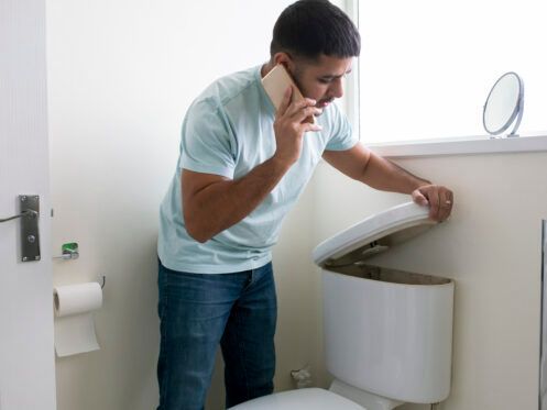 A man is talking on a cell phone while standing next to a toilet.
