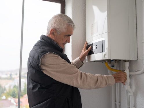 An older man is fixing a boiler in a room.